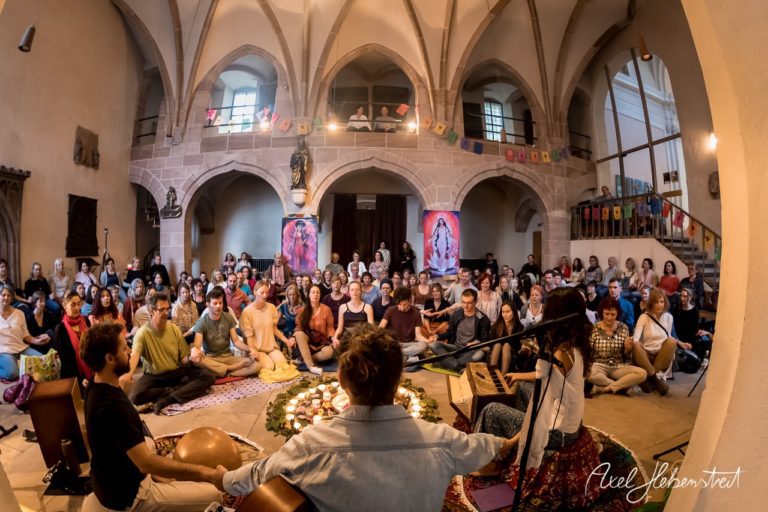 Eine große Gruppe von Menschen sitzt in einem harmonischen Raum während einer musikalischen Veranstaltung. – © Axel Hebenstreit
