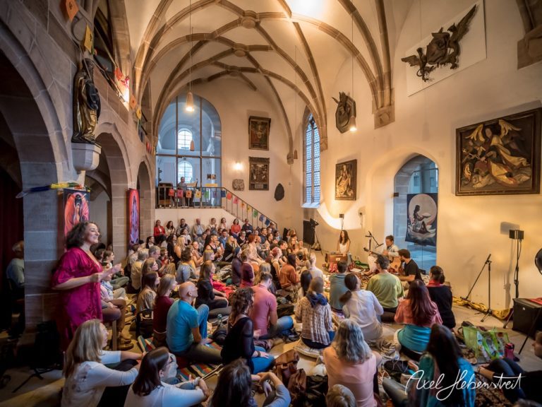 Eine große Gruppe von Menschen sitzt gebannt auf dem Boden und lauscht einem Musiker in einem historischen Saal. – © Axel Hebenstreit