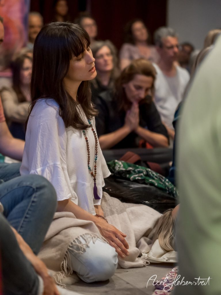Eine nachdenklich wirkende Frau sitzt im Yoga-Seminar, umgeben von einer entspannten Gruppe. – © Axel Hebenstreit