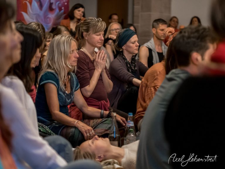 Teilnehmer einer spirituellen Versammlung sitzen in Stille und Konzentration in einem bunten Raum. – © Axel Hebenstreit