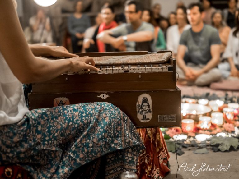 Eine Musikerin spielt auf einem Harmonium, während eine meditative Atmosphäre um sie herum auf einem Yoga-Event geschaffen wird. – © Axel Hebenstreit
