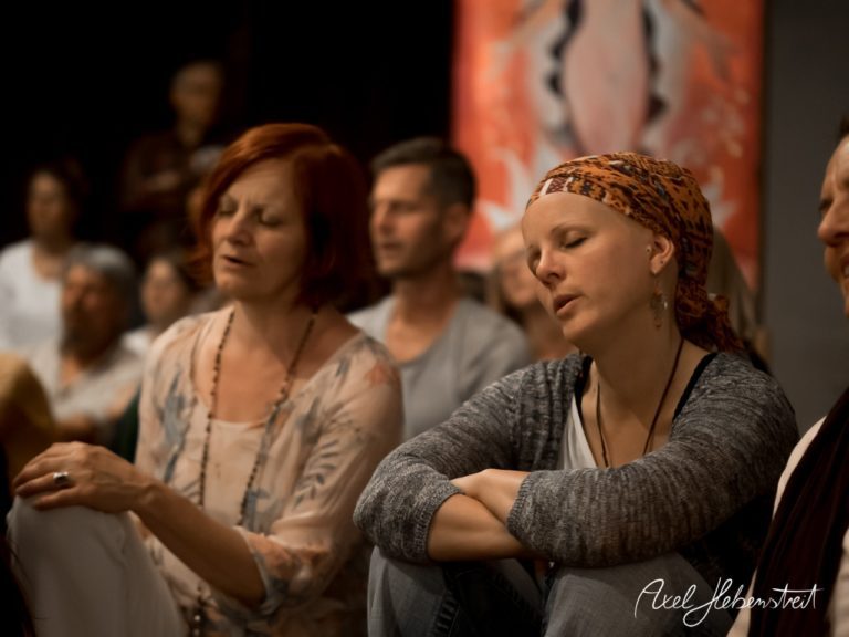 Eine Gruppe von Teilnehmern sitzt im Hintergrund, während sie meditieren und den harmonischen Klängen lauschen. – © Axel Hebenstreit