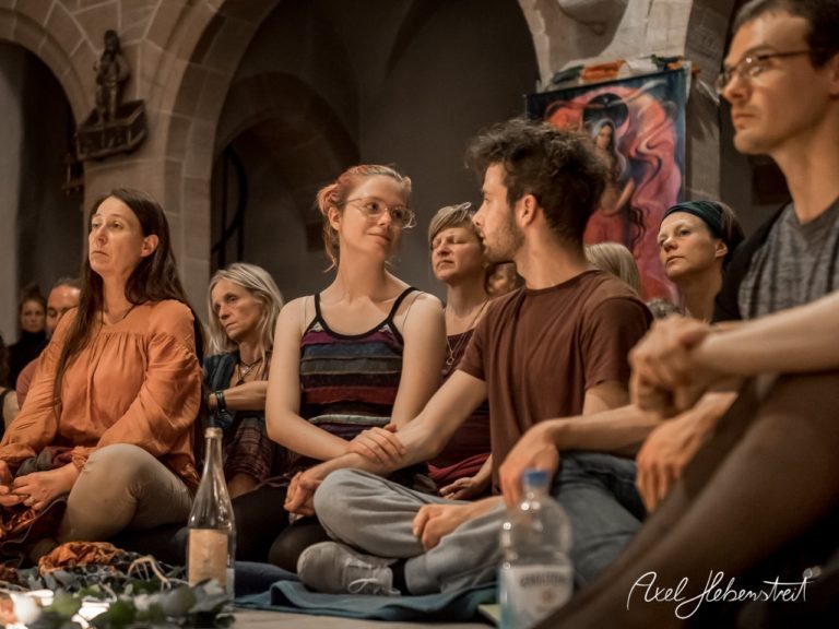 Eine Gruppe von Menschen sitzt in einem geschützten Raum, ihre Gesichter strahlen Verbindung und Achtsamkeit aus. – © Axel Hebenstreit