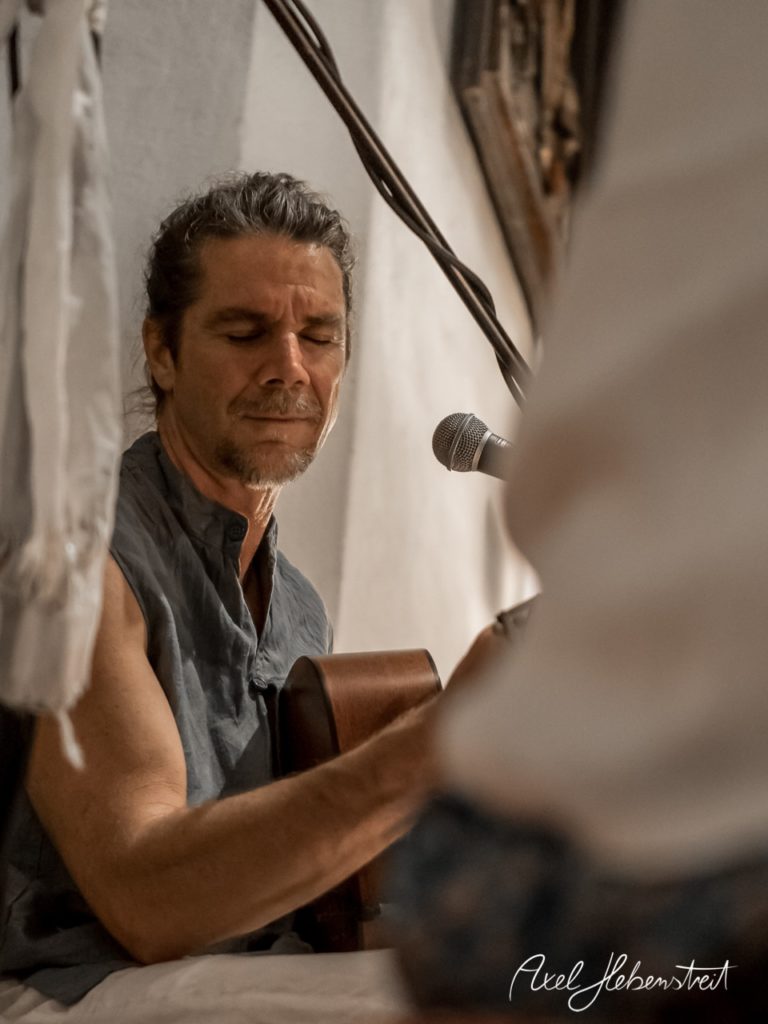 Ein Musiker spielt konzentriert Gitarre in einer intimen Umgebung, während das Licht sanft auf ihn fällt. – © Axel Hebenstreit