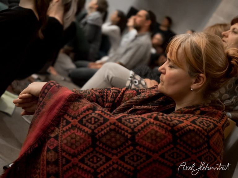 Frau in einer meditativen Pose, eingehüllt in eine Decke, während einer spirituellen Veranstaltung – © Axel Hebenstreit