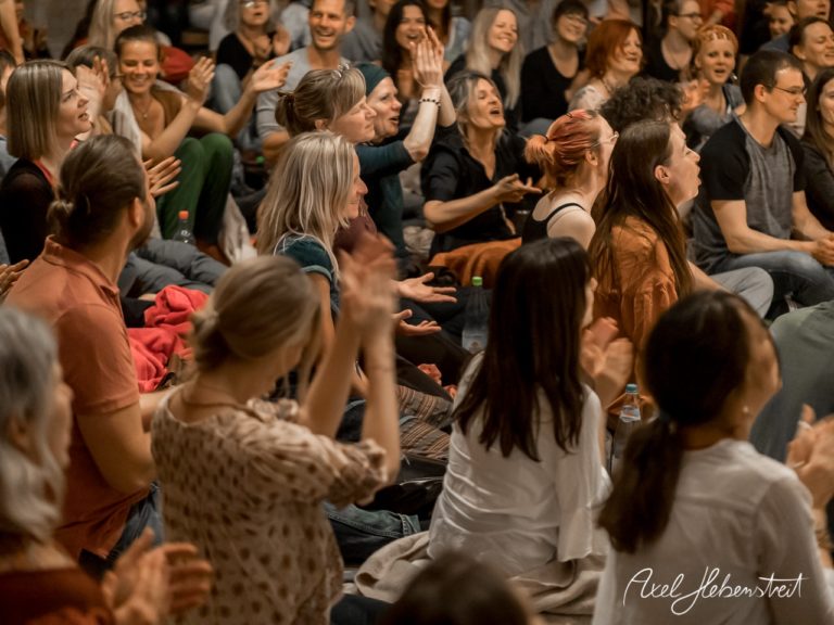 Eine jubilierende Menge sitzt auf dem Boden und applaudiert begeistert während einer Veranstaltung. – © Axel Hebenstreit