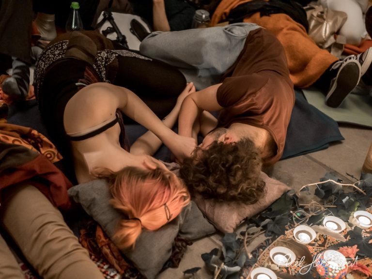 Junge Menschen liegen eng umschlungen auf Matten und Kissen, umgeben von Kerzenlicht und einer entspannten Atmosphäre. – © Axel Hebenstreit