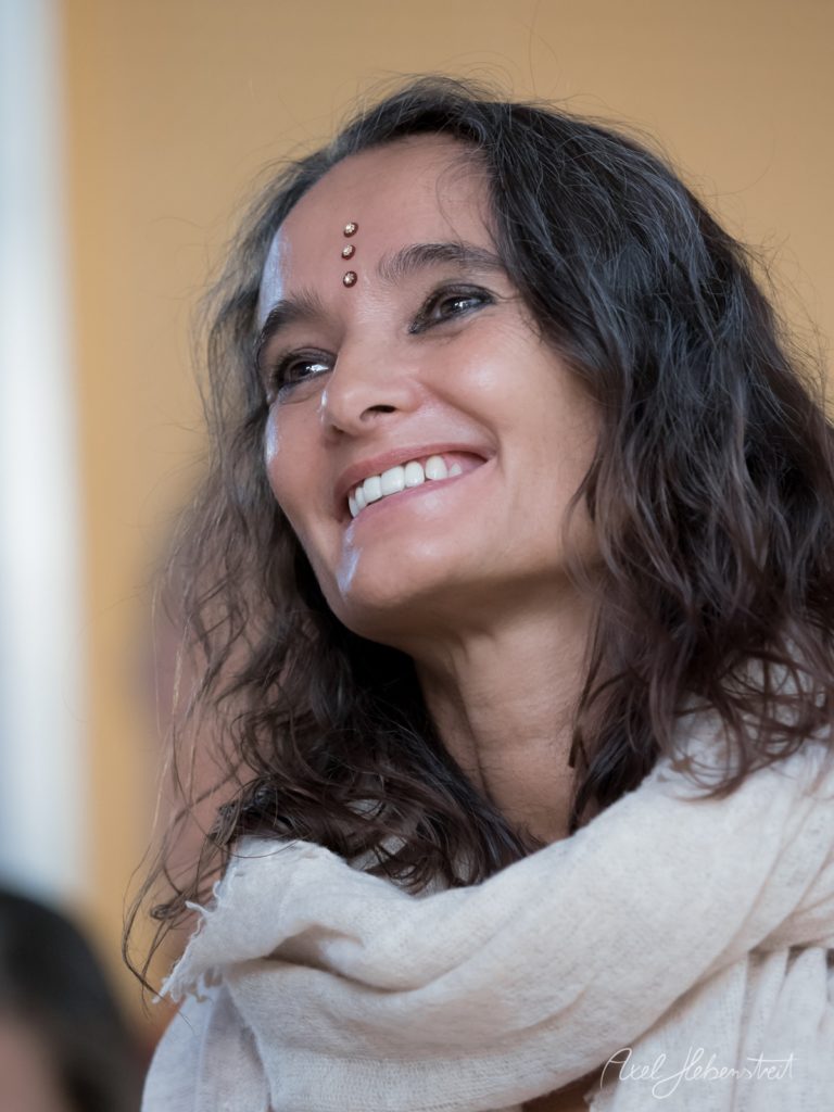 Porträt einer lächelnden Frau mit langen dunklen Haaren und Stirnpiercings vor neutralem Hintergrund – © Axel Hebenstreit