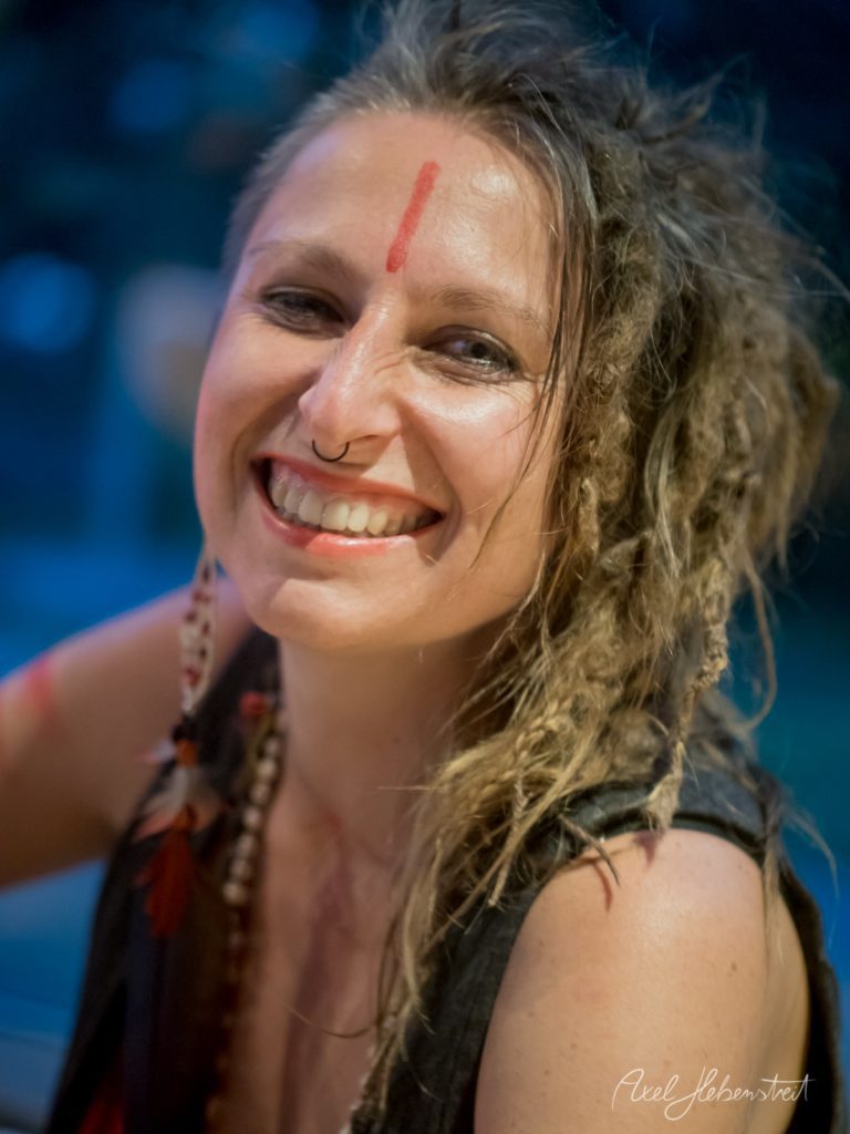 Lachende Frau mit Dreadlocks und rotem Tikka-Punkt vor blauem Hintergrund – © Axel Hebenstreit