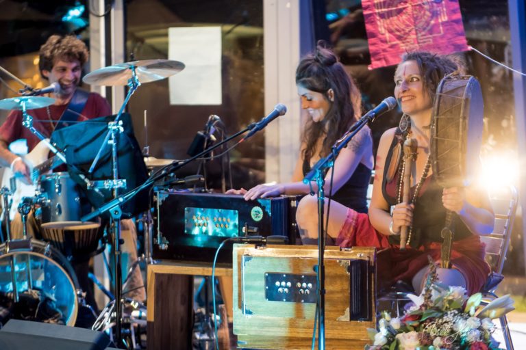 Liveband mit zwei Sängerinnen und Schlagzeuger bei Nachtauftritt in moderner Kulisse – © Axel Hebenstreit