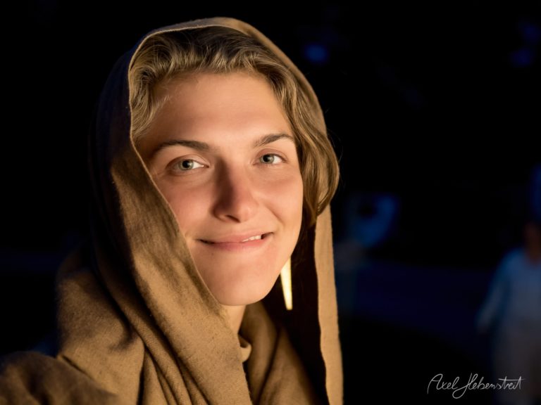 Porträt einer lächelnden Frau mit goldenem Kopftuch vor dunklem Hintergrund – © Axel Hebenstreit