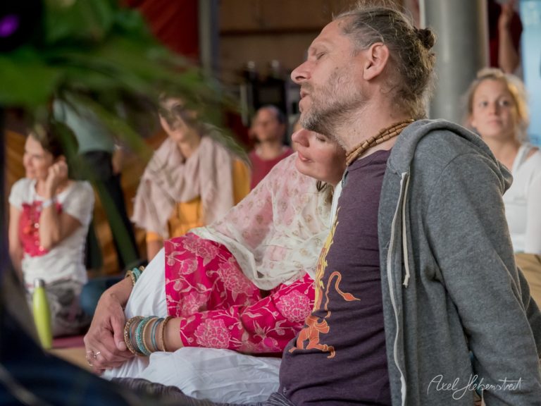 Ein Mann und eine Frau in traditioneller bayerischer Kleidung sitzen zusammen in einem Innenraum, während Zuschauer im Hintergrund beobachten – © Axel Hebenstreit