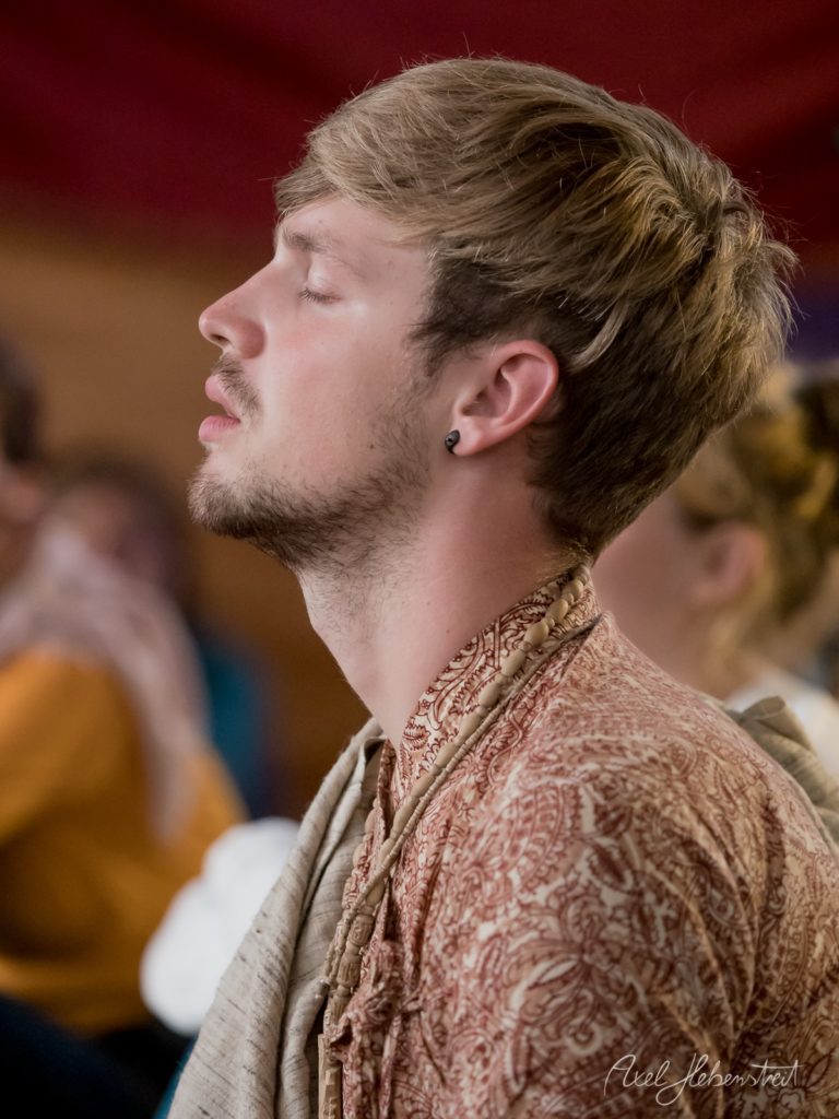 Mann mit lockigem Haar und Bart in traditionellem Gewand schaut konzentriert nach oben bei Veranstaltung – © Axel Hebenstreit