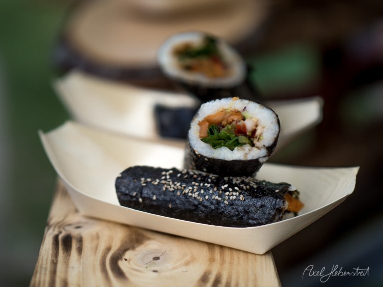Appetitlich angerichtete Sushi-Rollen mit schwarzem Noriblatt und Sesam auf weißem Porzellanteller auf Holzuntergrund – © Axel Hebenstreit
