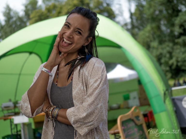 Lachende Frau vor grünem Zelt auf Festivalgelände mit Bäumen im Hintergrund – © Axel Hebenstreit