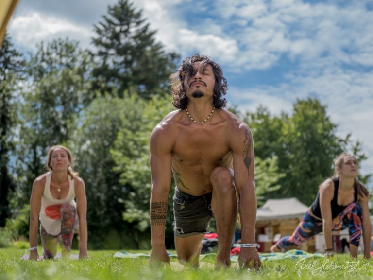 Gruppe beim Outdoor-Yoga in Plank-Position auf grüner Wiese mit Wald im Hintergrund – © Axel Hebenstreit
