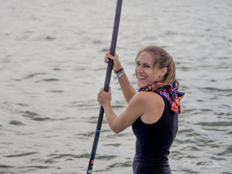 Lachende Frau mit Paddel beim Stand-Up-Paddling im Meer mit buntem Tuch – © Axel Hebenstreit