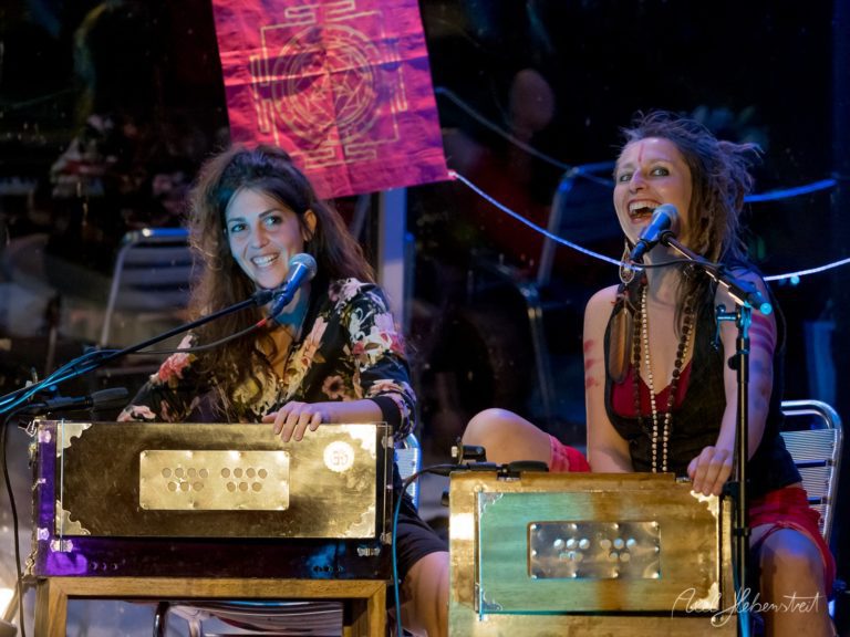 Zwei Musikerinnen performen auf der Bühne an handgefertigten Instrumenten mit energetischer Ausstrahlung unter bunter Beleuchtung – © Axel Hebenstreit