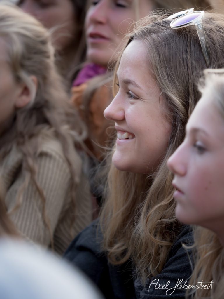 Lächelnde junge Frau in einer Gruppe, umgeben von einer entspannten Festivalatmosphäre. – © Axel Hebenstreit