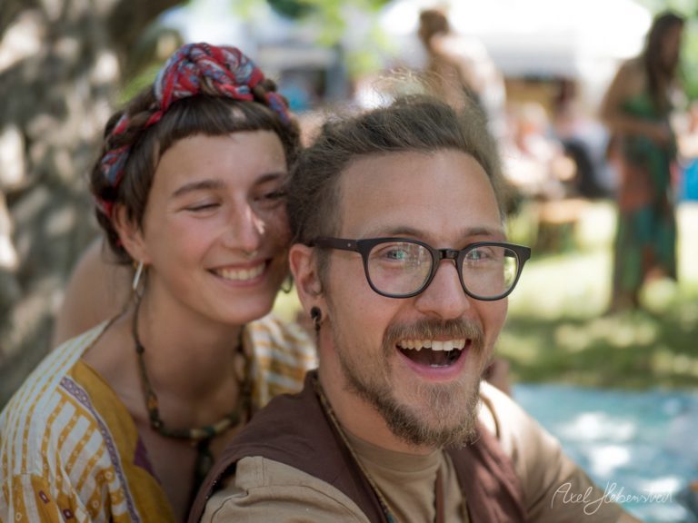 Zwei lachende Menschen posieren fröhlich bei einem Outdoor-Festival mit Pool im Hintergrund – © Axel Hebenstreit