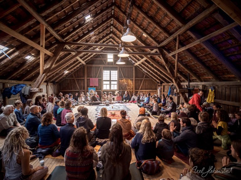 Große Gruppe von Menschen sitzt im Kreis in einer rustikalen Scheune bei einem gemeinschaftlichen Gathering – © Axel Hebenstreit