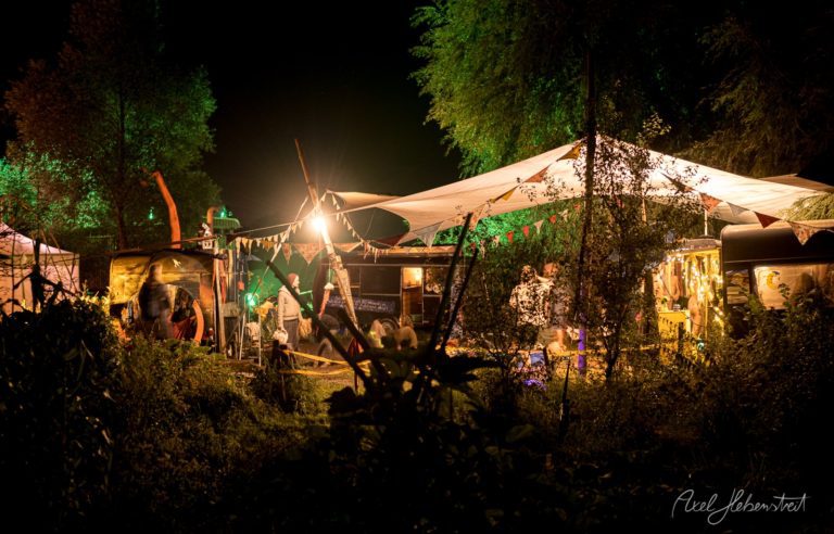 Nächtliches Outdoor-Festival in waldiger Umgebung mit beleuchteten Zelten, Bühne und Publikum – © Axel Hebenstreit