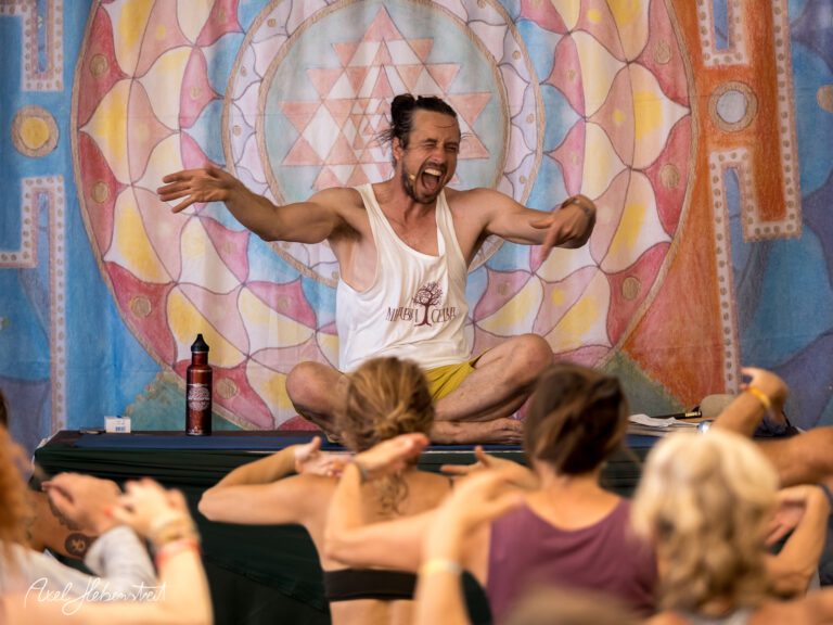 Ein leidenschaftlicher Yogalehrer leitet die Teilnehmer energetisch auf einer Bühne während einer Yoga-Sitzung – © Axel Hebenstreit