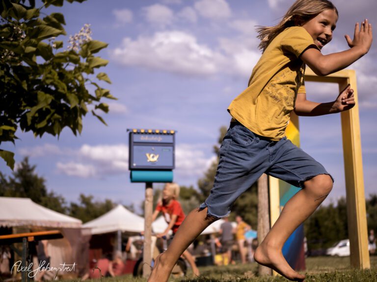 Ein fröhliches Kind läuft auf einer Wiese während eines Festivals im Freien. – © Axel Hebenstreit