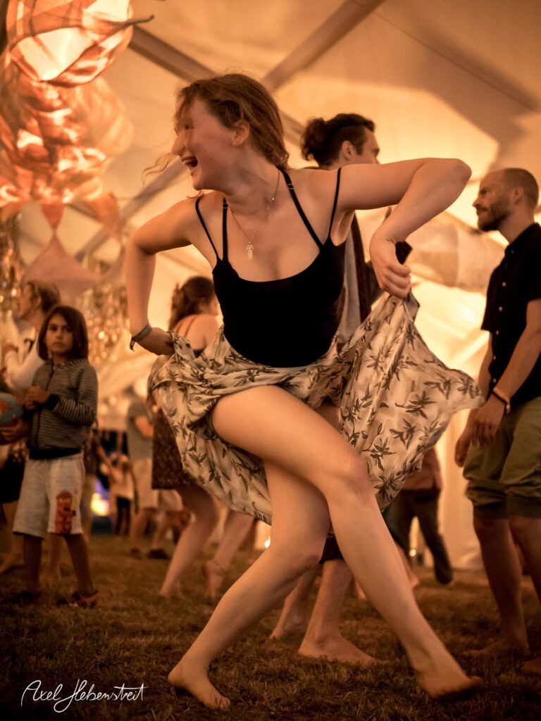 Eine fröhliche Tänzerin in festlicher Atmosphäre schwingt ihren Rock unter einem Zelt auf einem Festival – © Axel Hebenstreit