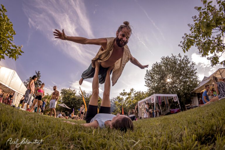 Akrobatische Darstellung eines Mannes, der über eine Frau auf einer Wiese in entspannter Festivalatmosphäre schwebt – © Axel Hebenstreit
