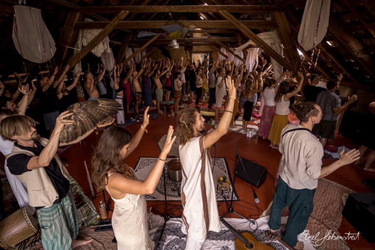 Gemeinschaftliche Meditationssitzung in einem liebevoll gestalteten Raum mit erhobenen Händen – © Axel Hebenstreit