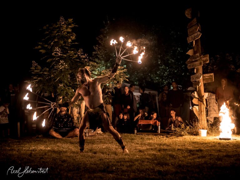 Feuerakrobatik bei Nacht, umgeben von faszinierten Zuschauern auf einem Festival. – © Axel Hebenstreit
