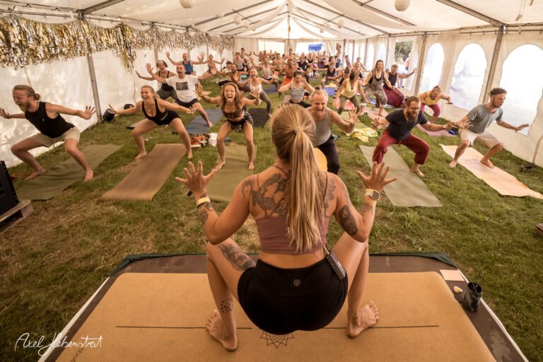 Yoga-Übungen in einem Zelt auf einem Festival, Teilnehmer konzentriert und energisch in der Gruppenpraxis. – © Axel Hebenstreit