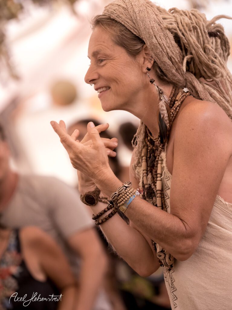 Lächelnde Frau mit Dreadlocks und Schmuck in fröhlicher Atmosphäre eines Festivals – © Axel Hebenstreit
