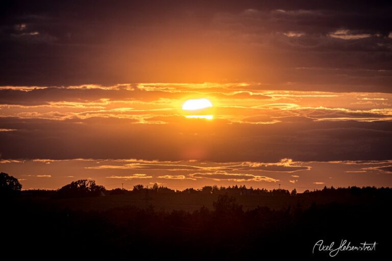 Sonnenuntergang hinter Wolken über einer bewaldeten Landschaft in Bayern – © Axel Hebenstreit