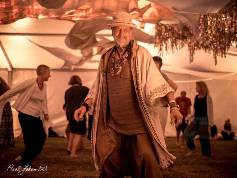 Tanzender Mann in einem festlichen Zelt, umgeben von fröhlichen Menschen, die eine spirituelle Atmosphäre genießen – © Axel Hebenstreit