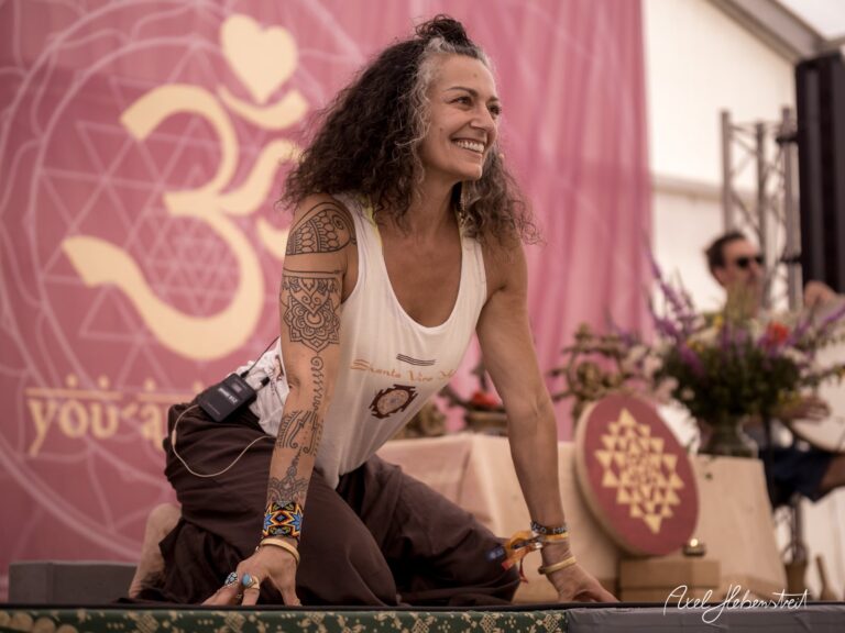 Yogalehrerin in entspannter Pose mit strahlendem Lächeln auf einem Festival – © Axel Hebenstreit