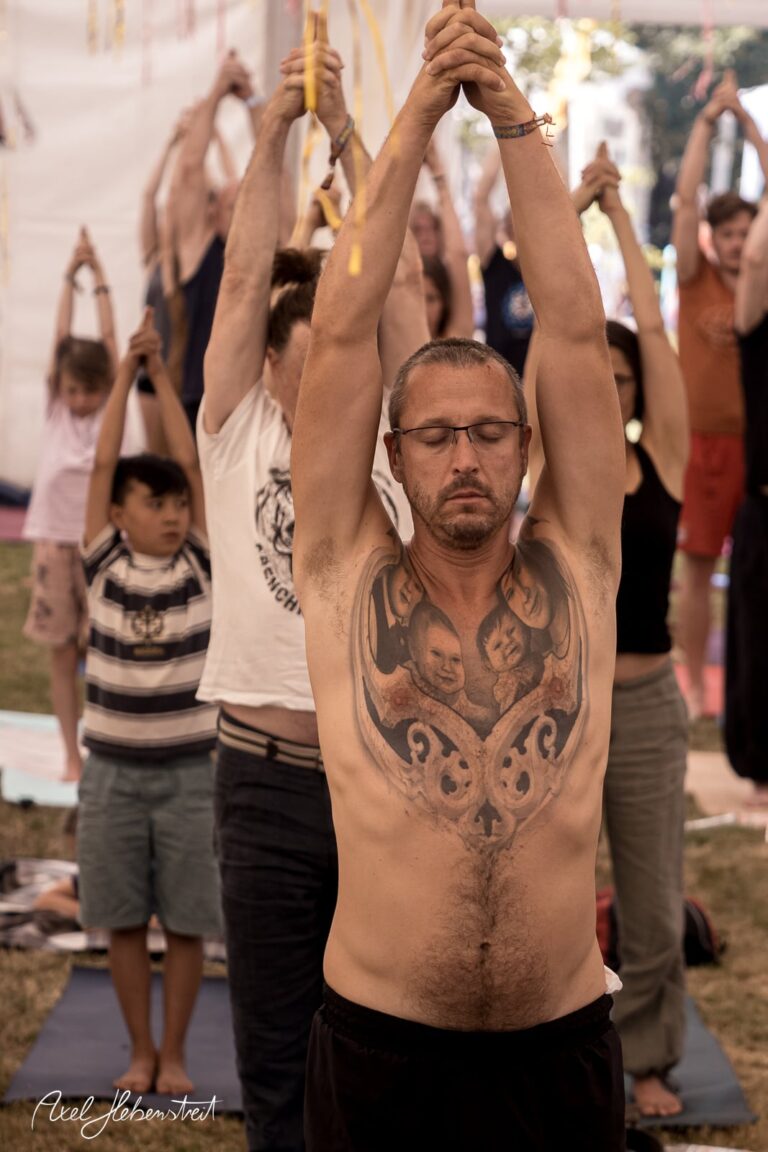 Mann mit beeindruckendem Tattoo aktiviert meditative Pose unter freiem Himmel bei einem Yoga-Event – © Axel Hebenstreit