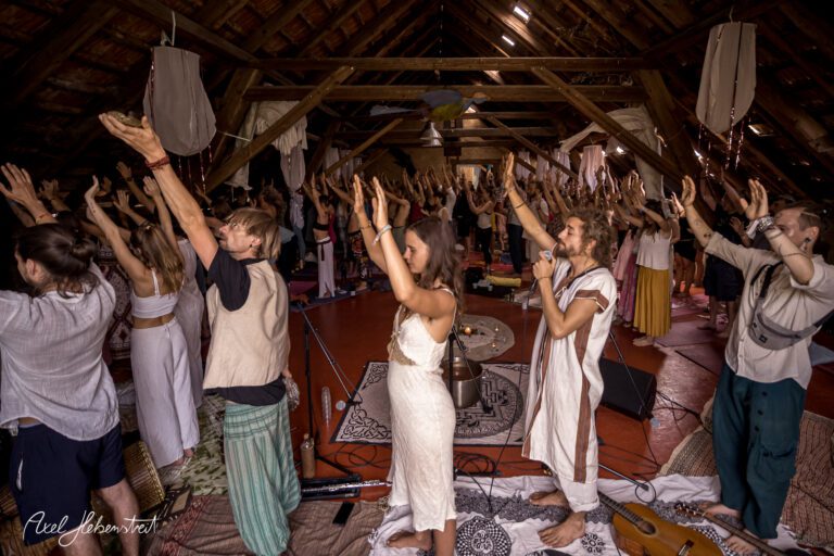Gemeinschaftlich meditierende Menschen mit erhobenen Händen in einer spirituellen Yoga-Umgebung – © Axel Hebenstreit