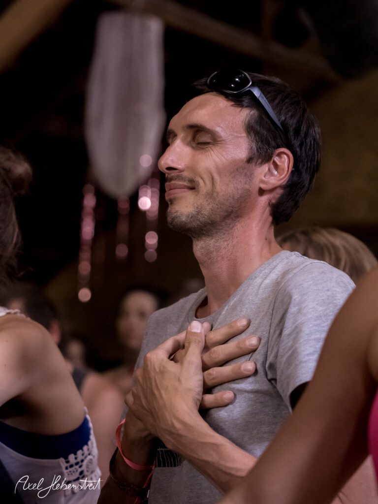Ein Mann mit geschlossenen Augen und einem ruhigen Lächeln, der in einer spirituellen Atmosphäre meditiert. – © Axel Hebenstreit