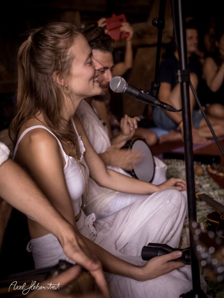 Junge Frau im weißen Outfit singt lächelnd ins Mikrofon bei einem intimen Musik-Event – © Axel Hebenstreit