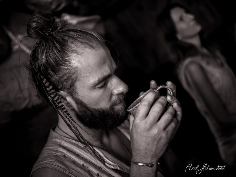 Ein Mann mit Zopf und Bart hält eine Tasse, vertieft in einen meditativen Moment. – © Axel Hebenstreit