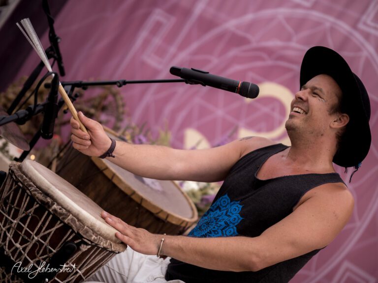 Ein Musiker spielt mit Begeisterung Trommel und singt auf einer Bühne bei einem Festival – © Axel Hebenstreit