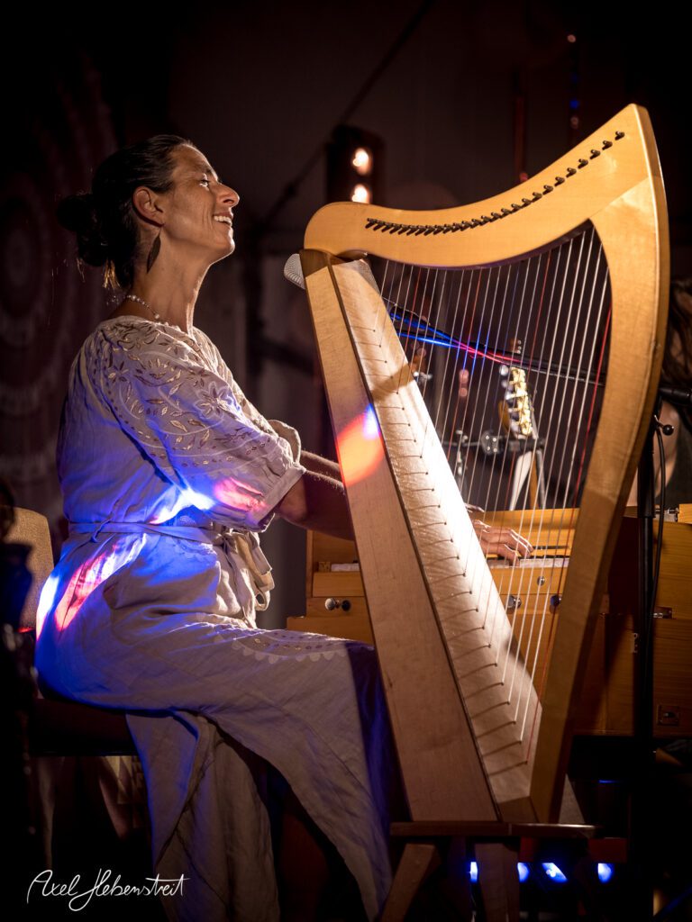 Frau spielt lächelnd Harfe bei einem Konzert, umgeben von stimmungsvollem Licht – © Axel Hebenstreit