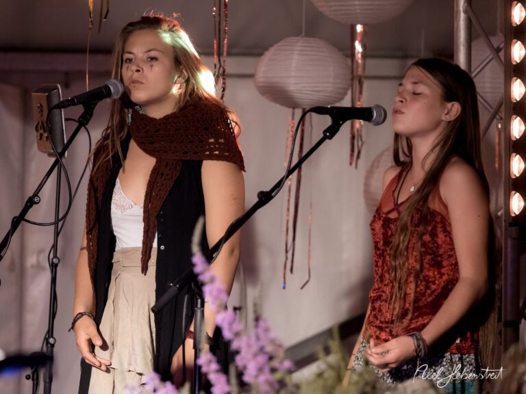 Zwei Sängerinnen performen auf einer Bühne, umgeben von stimmungsvollem Licht und Dekoration – © Axel Hebenstreit