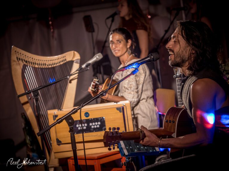 Musiker spielen gemeinsam live auf einer Bühne, umgeben von stimmungsvollem Licht und einem engagierten Publikum – © Axel Hebenstreit