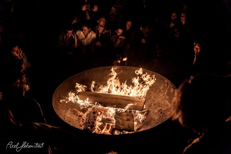 Ein Feuerkreis mit lodernden Flammen, umgeben von Menschen, die gebannt zuschauen – © Axel Hebenstreit
