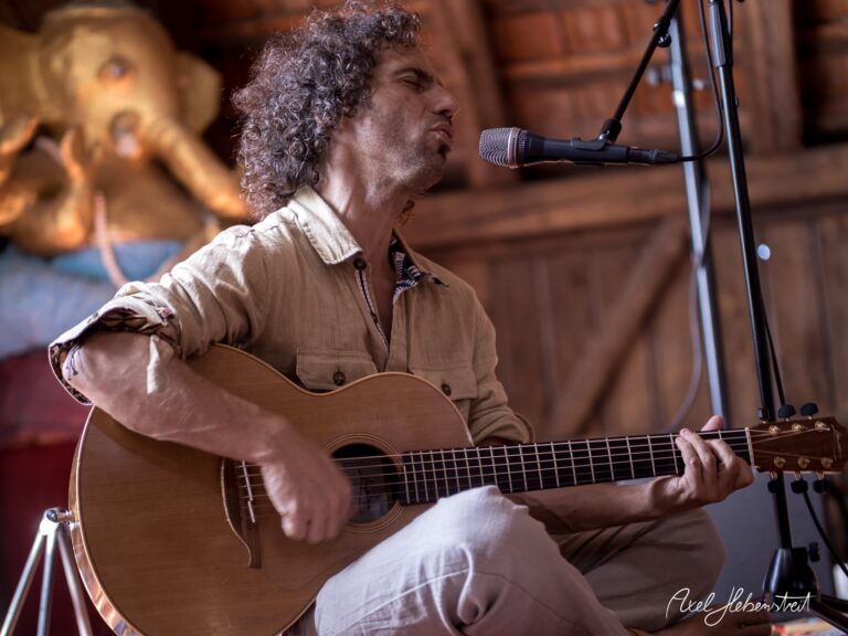 Ein Musiker singt emotional und begleitet sich auf der akustischen Gitarre in einer gemütlichen Location – © Axel Hebenstreit