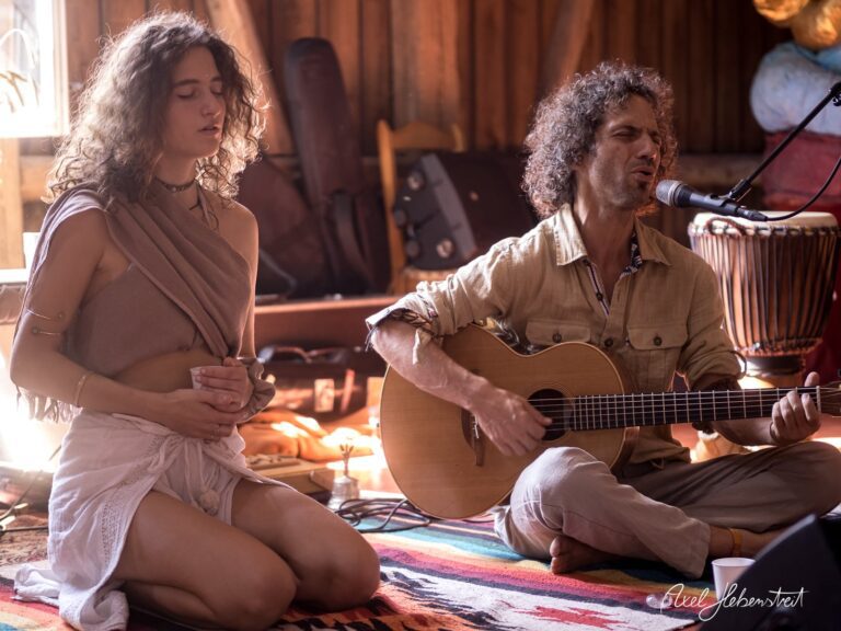 Zwei Menschen sitzen meditatativ in einem Holzraum, während einer Gitarre spielt und der andere in Stille verweilt – © Axel Hebenstreit