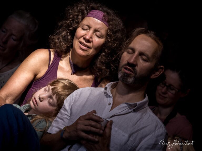 Eine ruhige Gruppe von Menschen, darunter eine schlafende Frau und ein Kind, in meditativer Stimmung bei einem Event – © Axel Hebenstreit